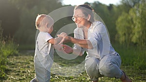 mom hugging baby son in nature. happy family kid dream concept. baby goes to mom in nature in the park hugs a parent in