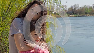 Mom is hugging her daughter by the river. A little girl with her mother by the water. Family in the open air.