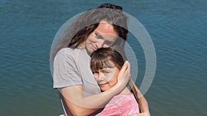 Mom is hugging her daughter by the river. A little girl with her mother by the water. Family in the open air.