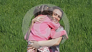 Mom hugs children in nature. Woman with little girls in a park on green grass. Family hugging on lawn.