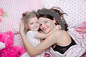 Mom hugs her daughter lying in bed