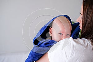 Mom hugs her little cutest baby after bath with blue towel on head. Infant child on mother hands. Mothercare love