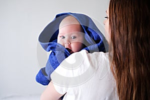 Mom hugs her little cutest baby after bath with blue towel on head. Infant child on mother hands. Mothercare love