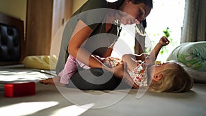 Mom hugs, kisses and tickles a little girl lying on the bed with her