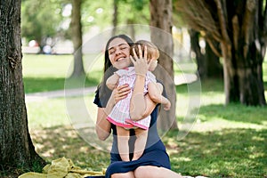 Mom hugs a little girl while sitting on a blanket on the lawn