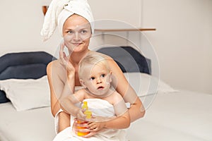 Mom and infant baby in white towels after bathing apply sunscreen or after sun lotion or cream. Children skin care in a hotel or