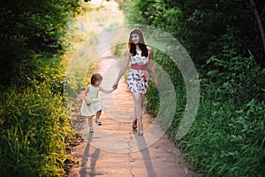 Mom keeps daughter's hand and walks the walk on the nature in sunset light