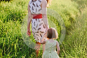 Mom keeps daughter's hand and walks the walk on the nature in sunset light