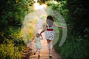 Mom keeps daughter's hand and walks the walk on the nature in sunset light