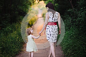 Mom keeps daughter's hand and walks the walk on the nature in sunset light