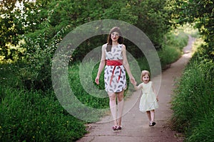 Mom keeps daughter's hand and walks the walk on the nature in sunset light