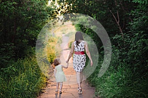 Mom keeps daughter's hand and walks the walk on the nature in sunset light