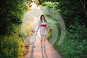 Mom keeps daughter's hand and walks the walk on the nature in sunset light