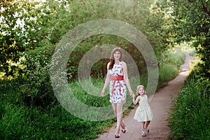 Mom keeps daughter's hand and walks the walk on the nature in sunset light