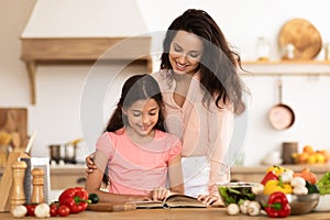 Mom and kid daughter looking through recipe book in kitchen