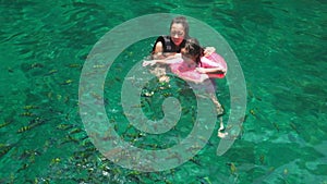 Mom and kid swim in the clear emerald sea.