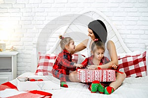 Mom and kids are laughing merrily while the older girl opens a Christmas gift