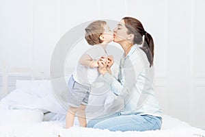 Mom kisses baby at home on the bed, the concept of family and children, mother`s day