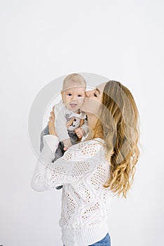 Mom kisses her baby on the cheek, the child smiles. Portrait on white background. Copy space. The concept of a happy motherhood
