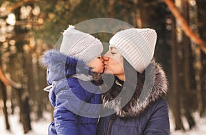 Mom kisses a little girl on a walk in the woods in winter. Motherly love