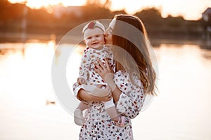 Mom kissing her little daughter near the lake on sunset. The concept of summer holiday. Mother`s, baby`s day. Family spending ti