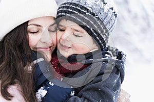 Mom kissing little stylish smiling happy cute boy, kid. Lovely family walking,activity in beautiful winter forest, park.Trees