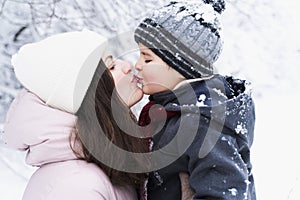 Mom kissing little stylish smiling happy cute boy, kid. Lovely family walking,activity in beautiful winter forest, park.Trees