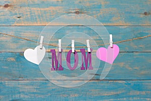 MOM letters. Mothers day message with hearts hanging with clothespins over blue wooden board