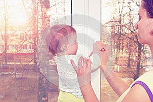 Mom and little baby girl close the window with a key.