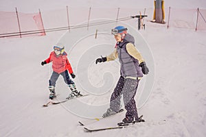 Mom and little boy mountain ski standing on top of the peak piste with high mountains on background