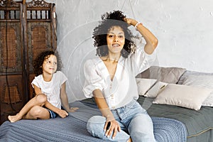 Mom and little cute curly girl spend time together, hugging and kissing each other