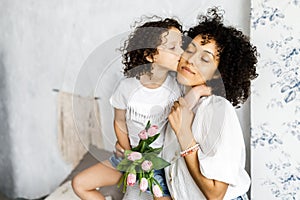 Mom and little cute curly girl spend time together, hugging and kissing each other