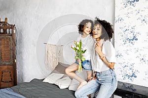 Mom and little cute curly girl spend time together, hugging and kissing each other