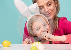 Mom with little cute girl are preparing for Easter. Mother and daughter wearing bunny ears are kissing. Easter banner