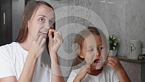 Mom and little daughter brush their teeth with dental floss at bathroom together