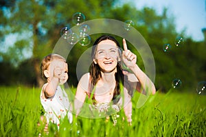 Mom and little daughter cheerfully catching soap bubbles