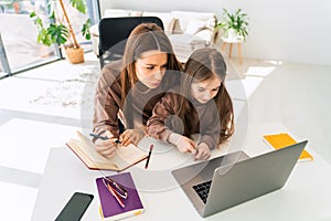 Mom and little daughter doing homework on laptop. Mother teaches the child at home.