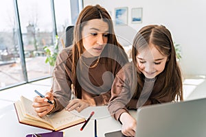 Mom and little daughter doing homework on laptop. Mother teaches the child at home.