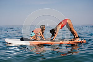 Mom and little daughter doing yoga on the paddle board