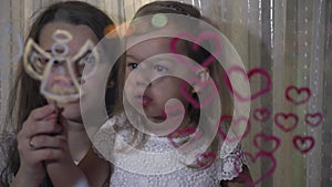 Mom with little daughter draw heart and angel paints on glass.