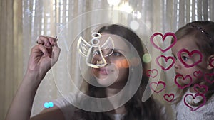 Mom with little daughter draw heart and angel paints on glass.