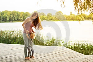 Mom and little daughter are fooling around on the pier near the lake. Learn to walk