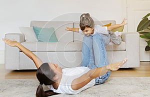 Mom and little daughter having fun together at home, playing airplane game
