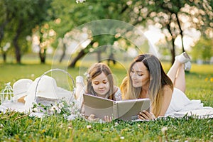 Mom and little daughter are looking at a family album with photos in the summer in the garden