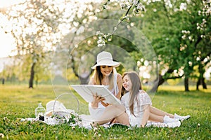 Mom and little daughter are looking at a family album with photos in the summer in the garden