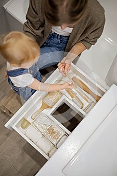 Mom and little daughter organizing bathroom storage, displaying beauty cosmetic creams and toiletries in drawer