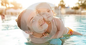 Mom and little daughter are played in the open swimming pool. Family with one child on vacation in warm countries. Positive people