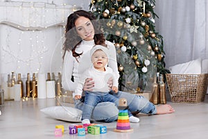 Mom with a little daughter playing on Christmas Eve on the background of a beautiful Christmas tree