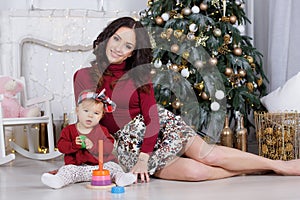 Mom with a little daughter playing on Christmas Eve on the background of a beautiful Christmas tree