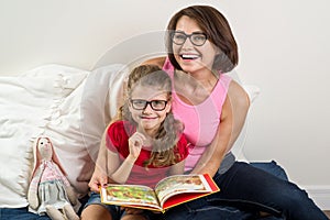 Mom and little daughter read book at home in bed.